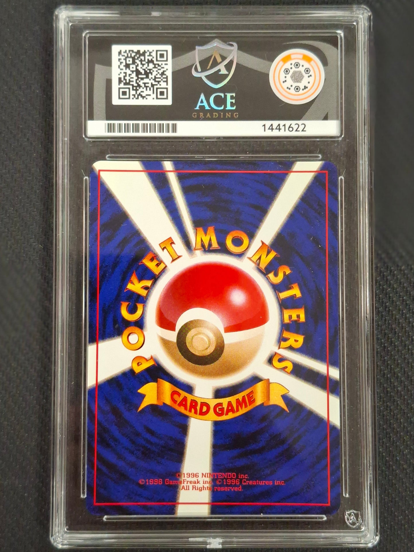 A graded Pokémon Trading Card Game card back in a clear plastic protective slab. The card features the classic blue and white sunburst design with a red and beige Pokéball logo in the center, and a black grading label at the top showing the ACE grading service and a QR code.